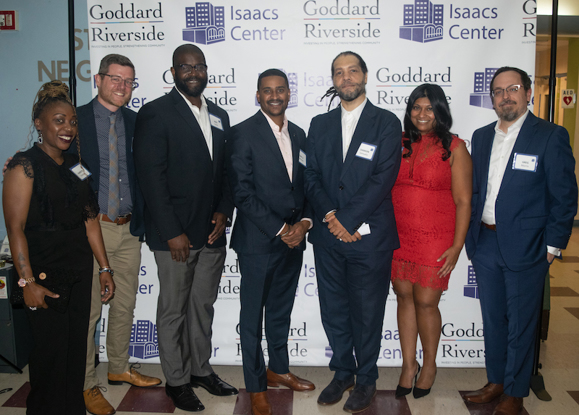 Leaders of the Isaacs Center and Goddard Riverside stand smiling in front of a banner bearing the logos of both organizations
