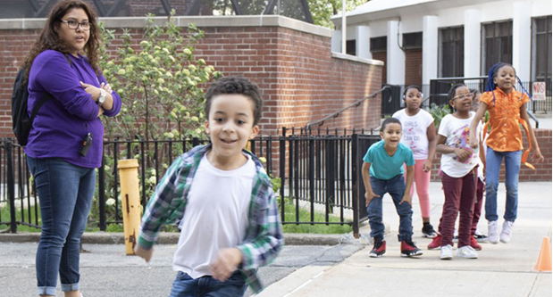 a child runs toward the camera, smiling, while other children wait at a starting line some distance behind him