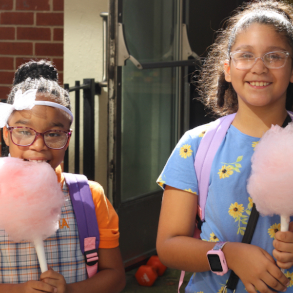 Two girls eat cotton candy while wearing new backpacks