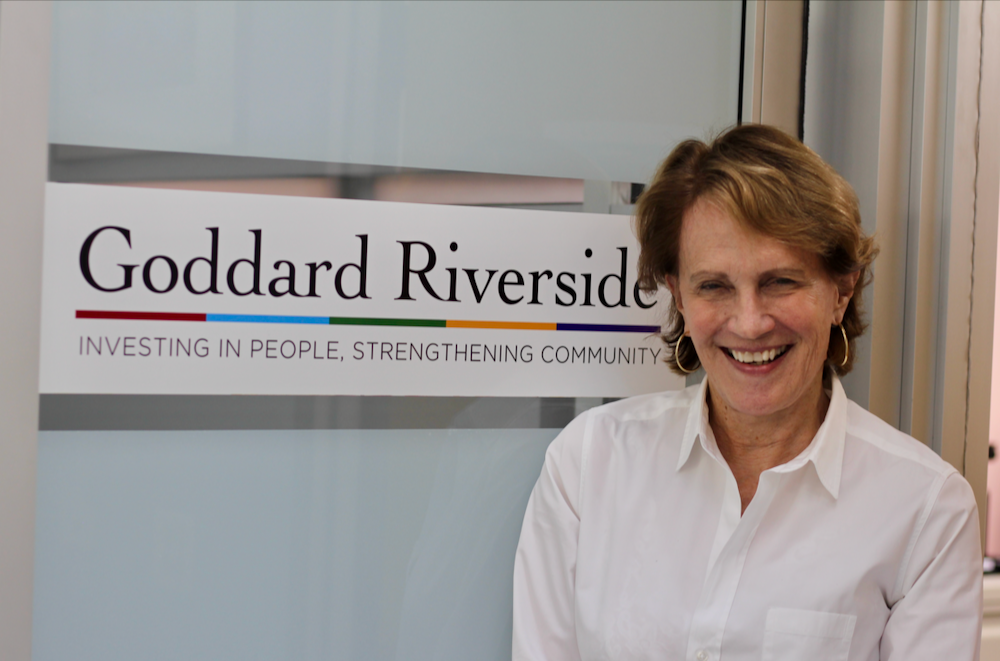 A woman smiles next to a Goddard Riverside logo