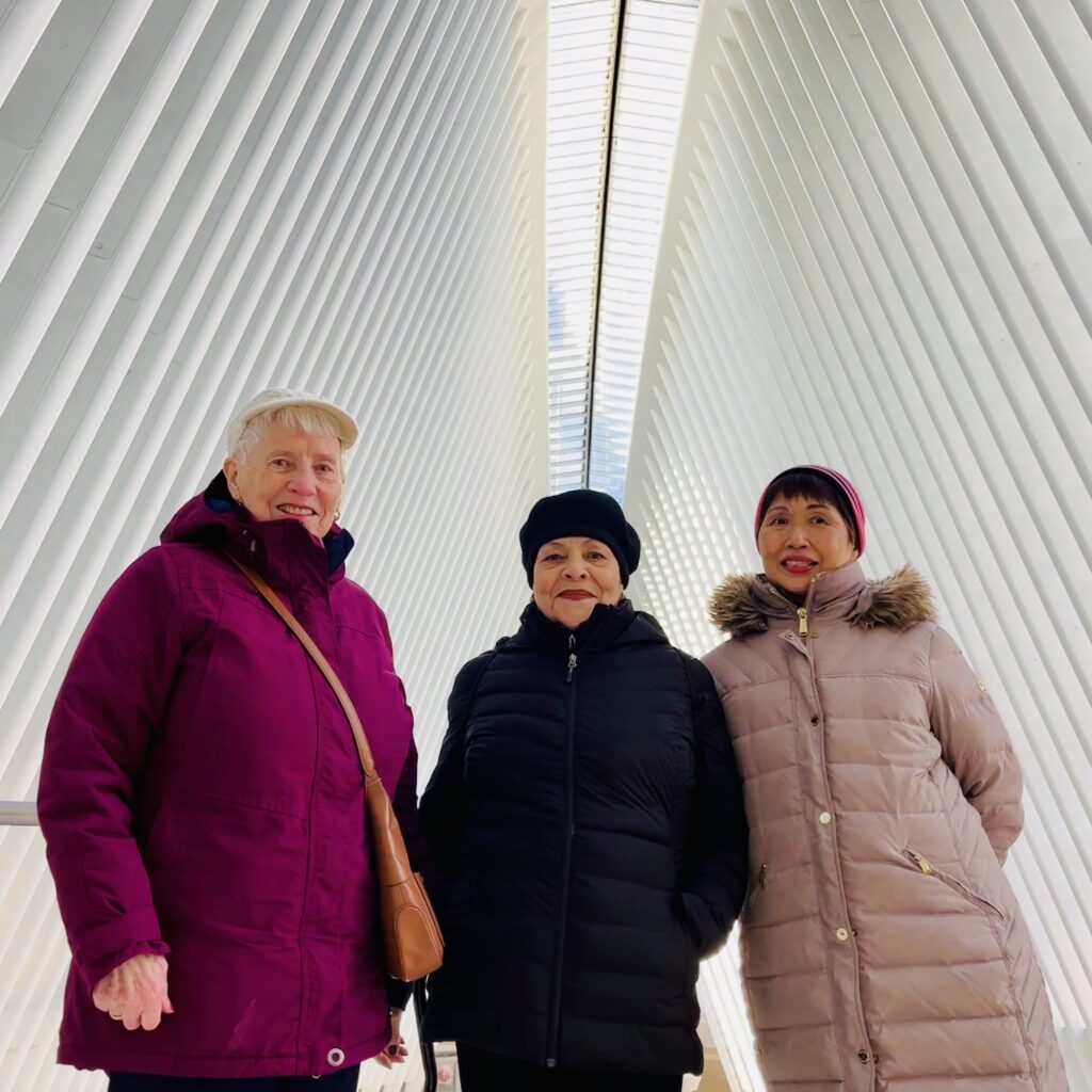 Three women in winter coats stand under a lofty ceiling of steep white ribs with a narrow skylight at the center
