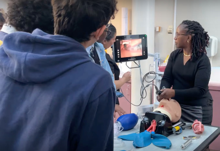 Students watch as a doctor demonstrates how to place a breathing tube in a medical mannequin