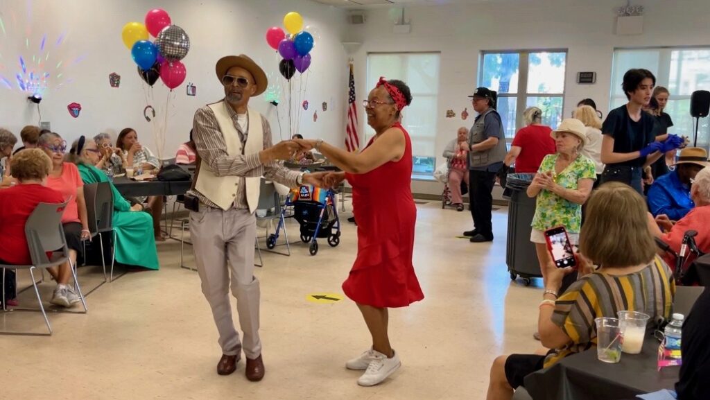 A couple dancing surrounded by other older adults in a festively decorated room