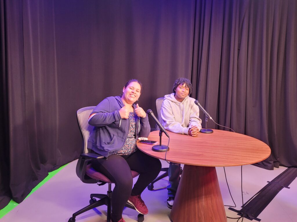 Two people at a tv set table posing for the camera