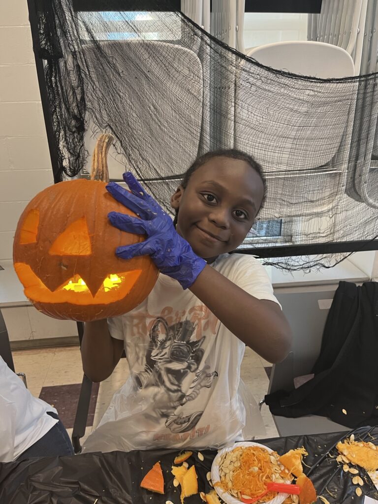 Child with gloves holding a jack-o-lantern