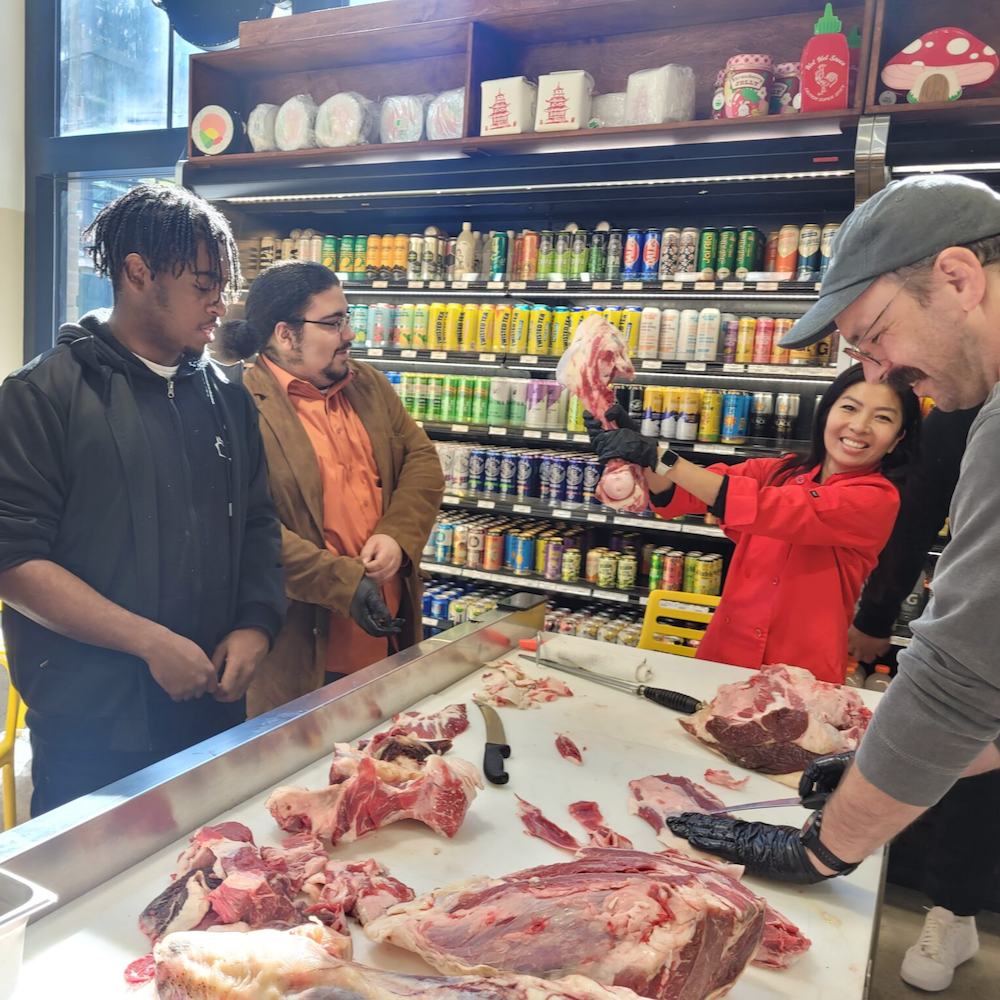 Young people look on as a butcher points to a cut of meat