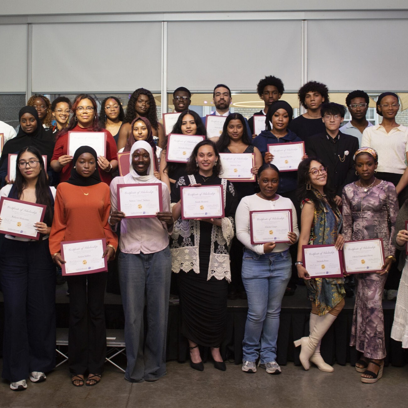About two dozen young people standing in rows holding up certificates